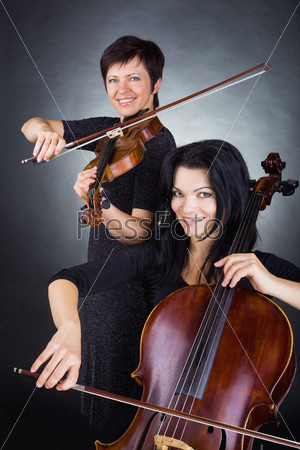 Two beautiful woman playing the violin on dark background