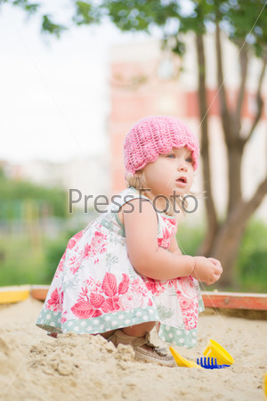 Adorable toddler girl in dress play with sand on sandbox