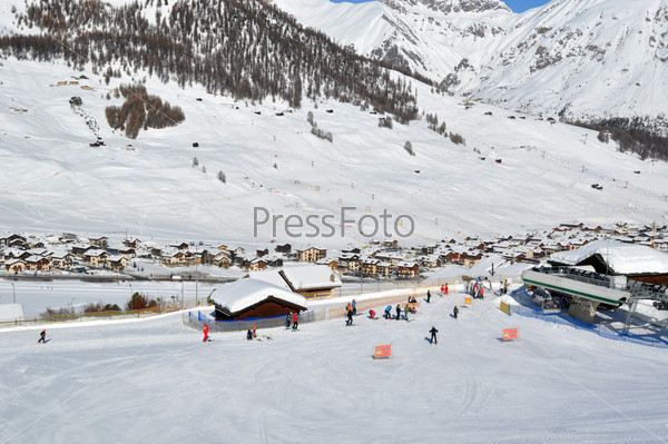 Ski scenario: Skiers approaching chairlift, mountains and village in the background - shot in Livigno, Italian Alps