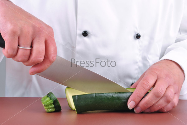 Female chef cut one zucchini with a kitchen knife, stock photo