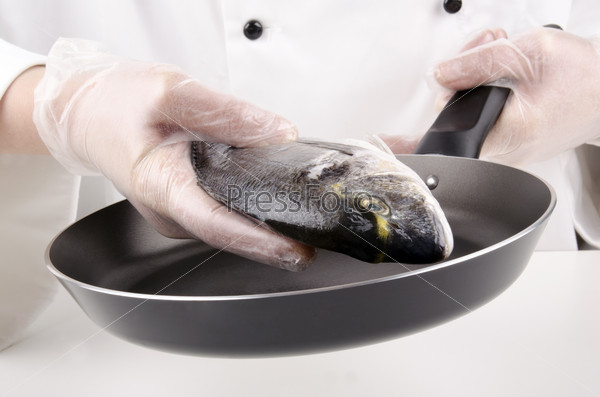 Female chef puts a sea bream for frying in a pan