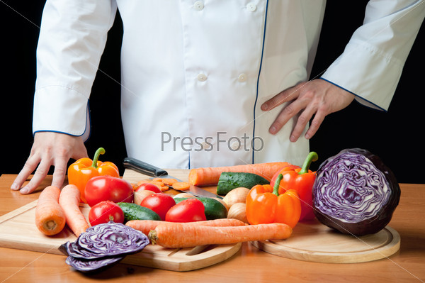 Food preparation: chef standing by the table with variety of fresh vegetables