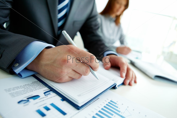Unrecognizable business person analyzing graphs and taking notes