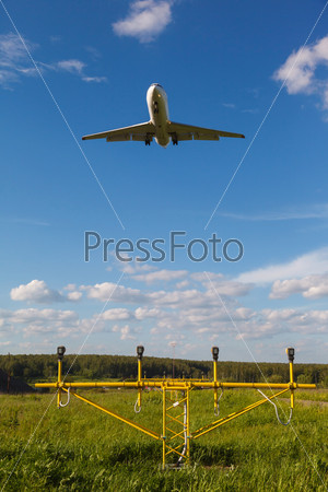 white plane with the gear against the blue sky and landing lights and green grass