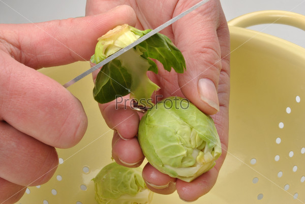 Руки чистят брюссельскую капусту ножом