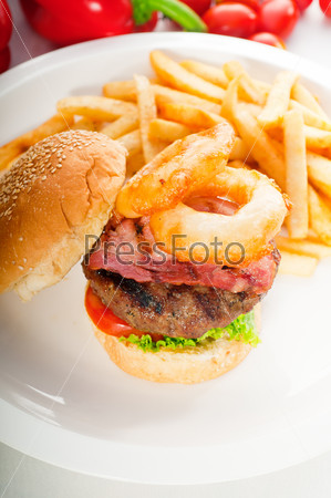 classic american hamburger sandwich with onion rings and french fries,with fresh vegetables on background