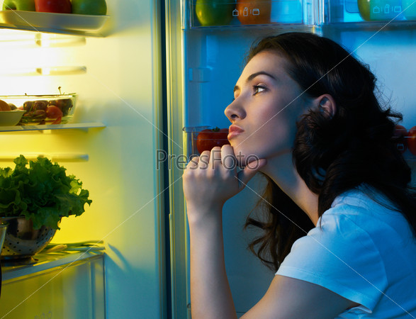 Молодая женщина грустно смотрит на содержимое холодильника