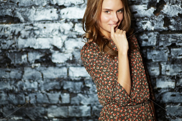 Girl with a flirty look leaning against a grunge brick wall and smiling at camera