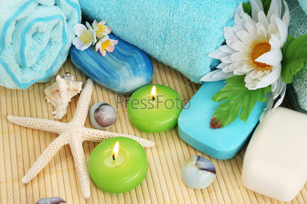 Stack of towels, soaps, candles, stones, flowers on mat background.