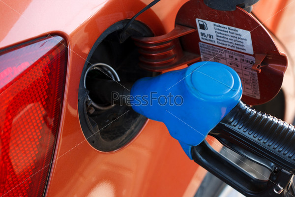 Orange car at gas station being filled with fuel, stock photo