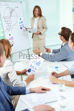 Happy top manager standing by the whiteboard and interacting with business partners at seminar