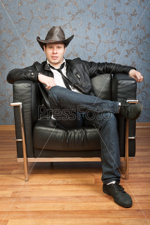 Young cowboy sitting in a chair against a background of patterned walls