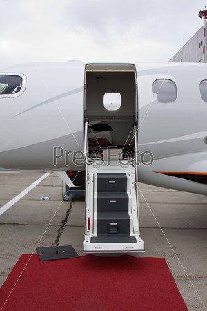 white private jet and open ladder, red carpet at the airport on a background cloudy sky