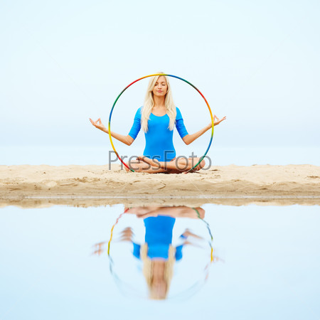 outdoor portrait of young beautiful blonde woman gymnast exercising with hoop on the beach