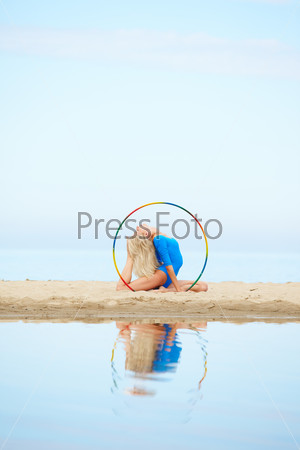 outdoor portrait of young beautiful blonde woman gymnast working out with hula-hoop on the sand