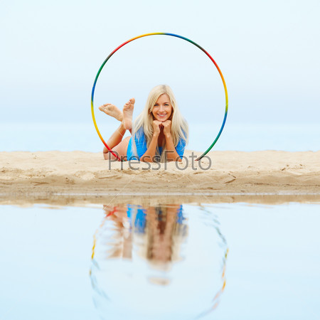 outdoor portrait of young beautiful blonde woman gymnast working out with hula-hoop on the beach