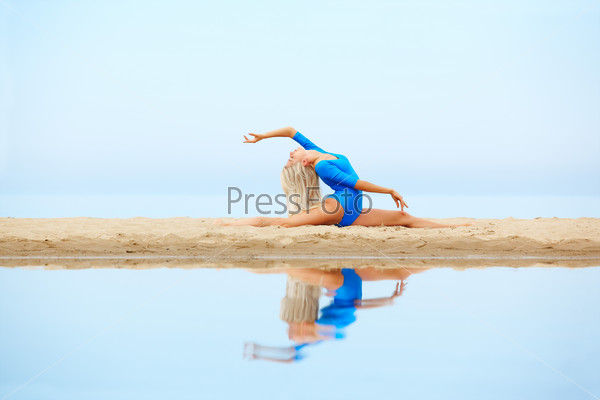 outdoor portrait of young beautiful blonde woman gymnast training on the beach