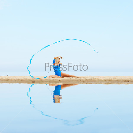 outdoor portrait of young beautiful blonde woman gymnast exercising with ribbon on the beach
