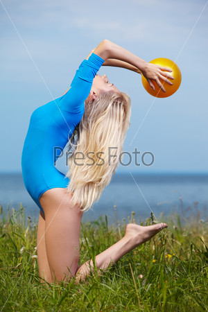 outdoor portrait of young beautiful blonde woman gymnast training with ball on green grass