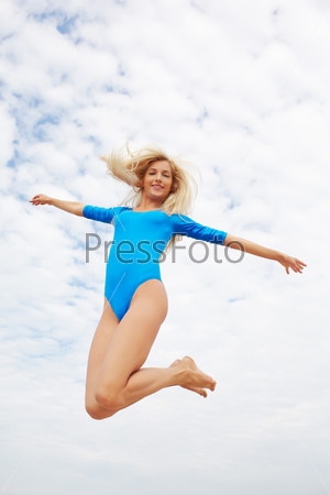 outdoor portrait of young beautiful blonde woman gymnast jumping in cloudy sky