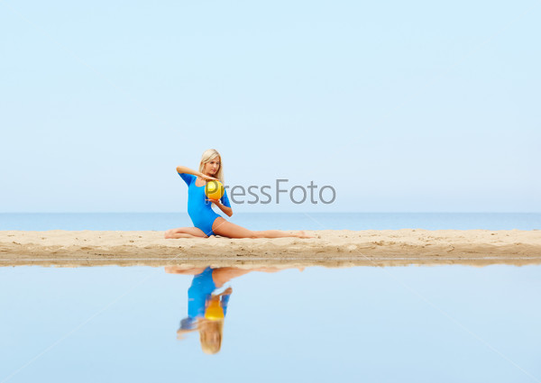 outdoor portrait of young beautiful blonde woman gymnast training with ball on the beach