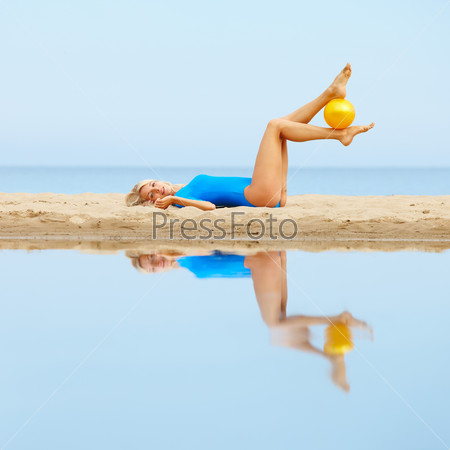 outdoor portrait of young beautiful blonde woman gymnast exercising with ball on the beach