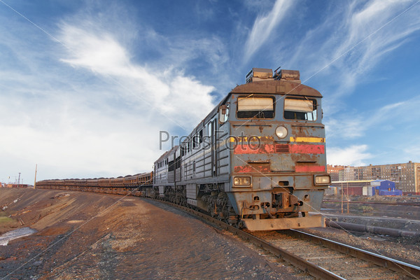 Front view of a locomotive with wagons hitched, illuminated by the setting sun.