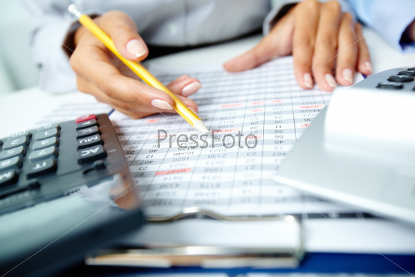 Photo of human hands holding pencil and marking numbers in documents