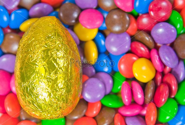 one yellow easter egg on a background of chocolate smarties