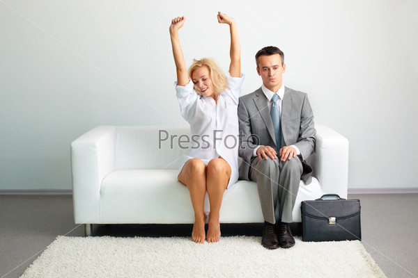 Sensual young lady in male shirt stretching herself sitting next to a tensed businessman after a night together