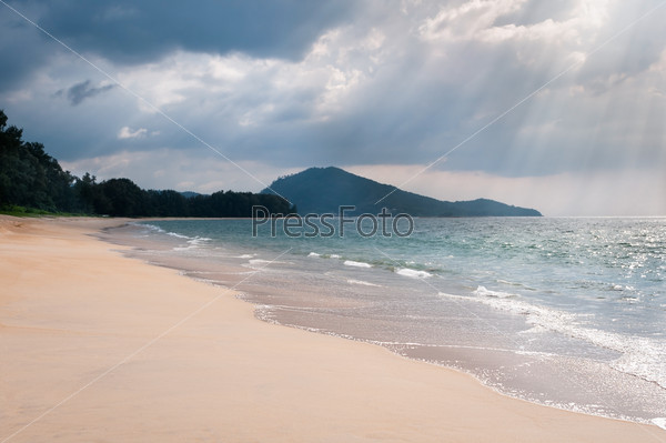 Heavy storm clouds and sunbeams under tropical sandy sea coast with clear blue water