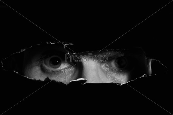 Scary eyes of a man spying through a hole in the wall, stock photo