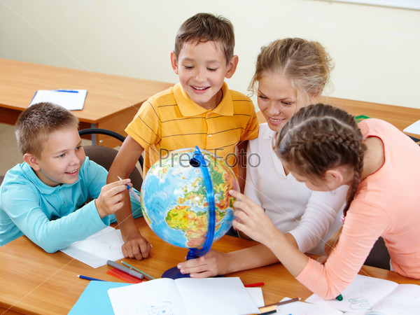 Portrait of cute schoolchildren and teacher looking at globe in classroom