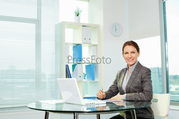 Cheerful business lady smiling at camera while sitting at her workplace
