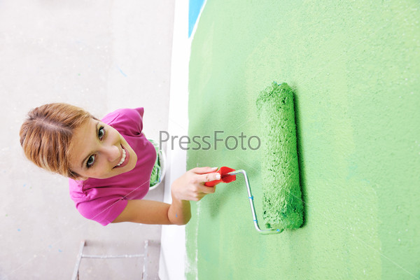 happy smiling woman painting interior white  wall in blue and green color of new house
