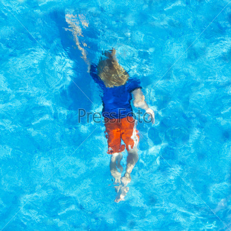 Young child swimming with his clothes on under water, seen from above