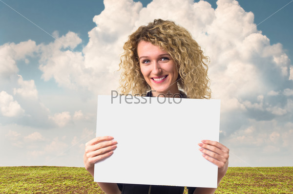 Attractive young business woman with curly hair holding a blank poster against rural background.