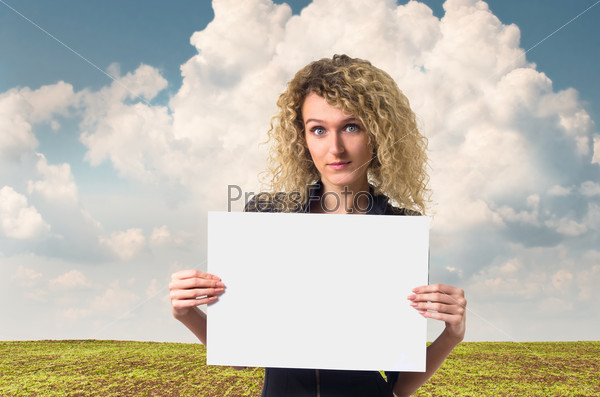 Attractive young business woman with curly hair looking with hope holding a blank poster against rural background.