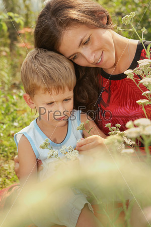 Baby and mom in the summer outdoors/Young woman with a little son treated flowers. Summer, sunny day.
