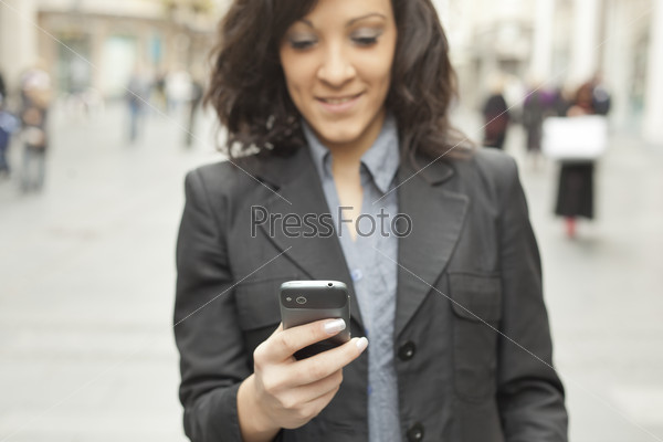 Young Woman with smartphone walking on street, downtown. In background is blured street. Phone in focus