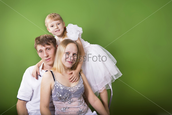 Young European family from three persons - mother, father and daughter. On a green background.