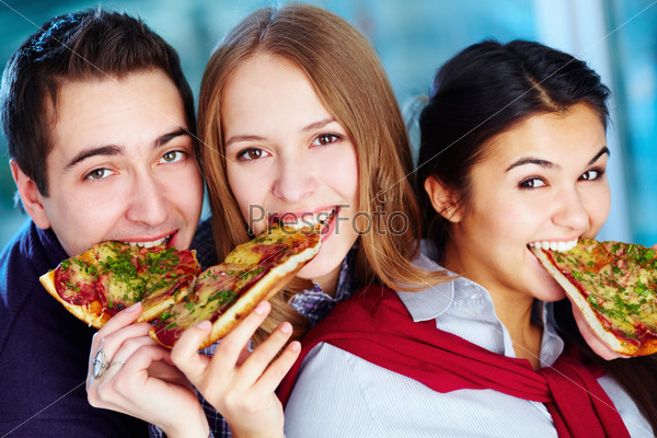 Image of happy teenage friends eating pizza and looking at camera