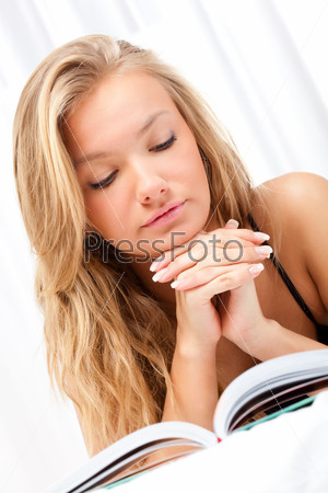 beautiful blonde woman laying on bed and reading book over white