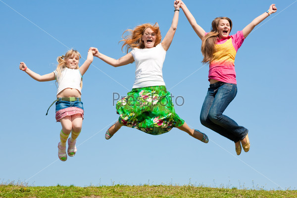 Happy Mom and two daughter jumping on green meadow