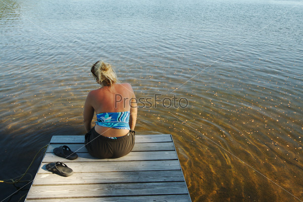 Beautiful lake scene with woman relaxing on the boat dock.