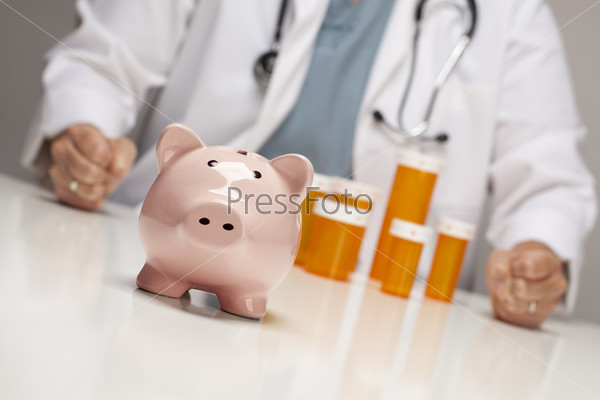 Doctor Wearing Stethoscope with Fists on Table Behind Medicine Bottles and Piggy Bank.