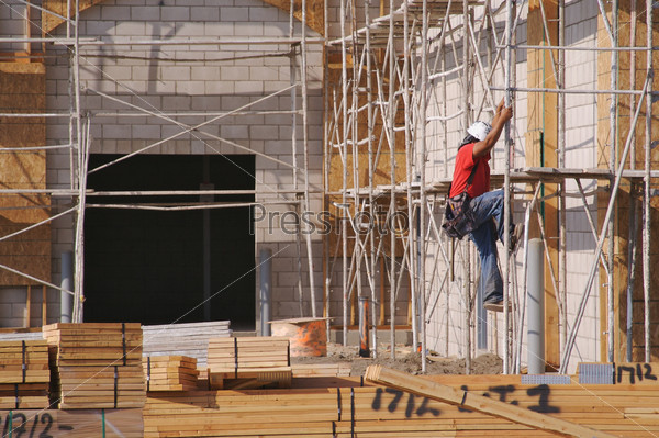 Carpenter climbing down scaffolding at a construction scene.