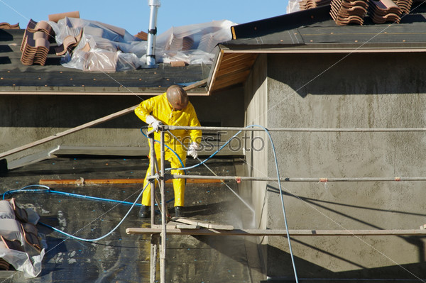 Construction worker pressure washes fresh applied surface of new home exterior, stock photo