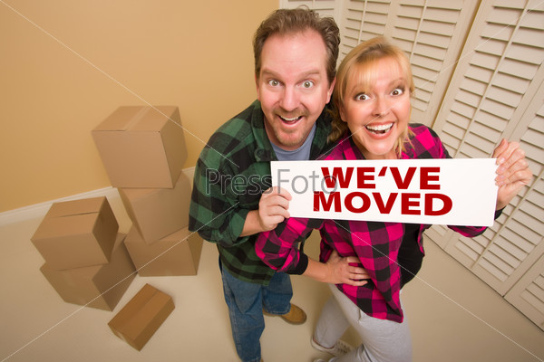 Goofy Couple Holding Coming Soon Sign in Room with Packed Cardboard Boxes.