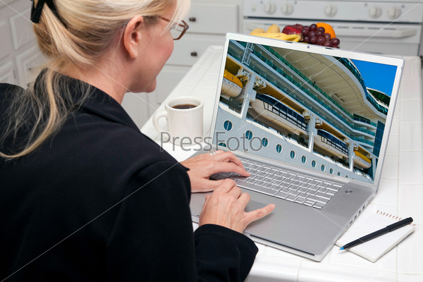 Woman In Kitchen Using Laptop to Research Travel, Vacation and Cruises. Screen image can easily be replaced using the included clipping path.